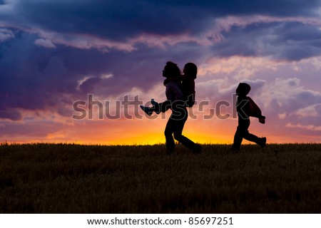 A woman carries her daughter on her back as her son walks behind at sunset.