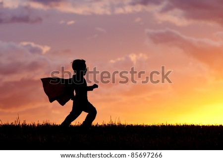A young boy wearing a cape plays a super hero at sunset.