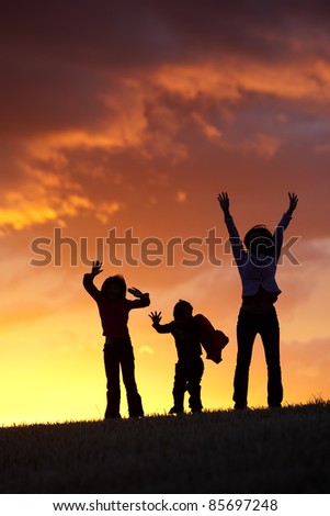 A woman and her two kids jump for joy at sunset.