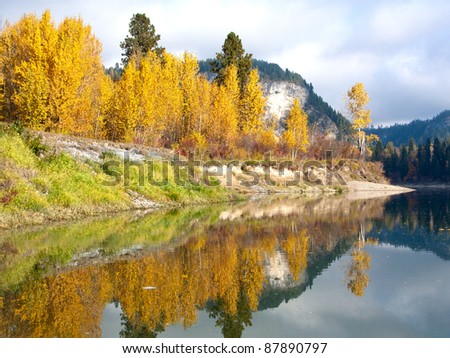The yellow and green colors of Autumn reflect off the calm still water of the river.