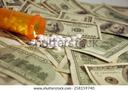 A prescription bottle of white pills spilling on a pile of $100 dollar bills