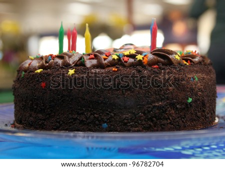 Chocolate layer cake with red, yellow, blue and green candles, star sprinkles on blue tablecloth.