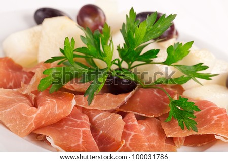 Smoked meat beef slices with melon cubes and grapes on ceramic plate