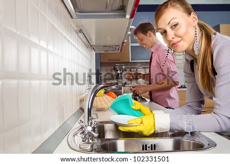 View of  young woman washing dishes and  man cooking at her in kitchen