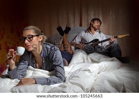 Happy boyfriend with electric guitar - playing and woman drinking coffee with pleasure on bed