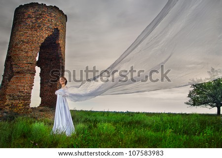 Bride with long veil staying against abandoned ruins in the evening