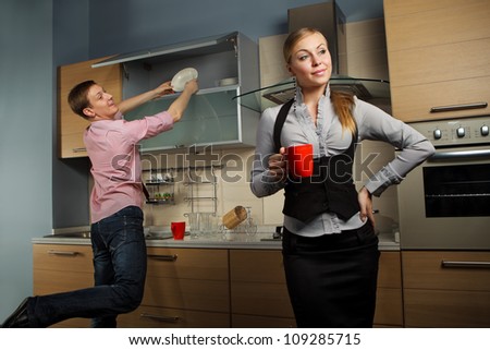 Young man washing dishes and his girlfriend drinking coffee in kitchen