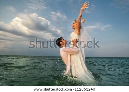 Romantic newly-married couple enjoying a summer vacation. Young groom lifting his bride in sea