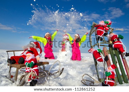 Two young women throwing snow on blue sky and sculpting snowman in street in wintertime