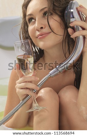 A young beautiful  woman is enjoying a bath with a glasses of champagne and talking by bath tub like by phone. - stock photo