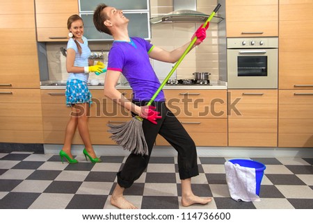 Modern kitchen - woman with sponge and smiling young man cleaning the floor at home and pretend to sing song with mop