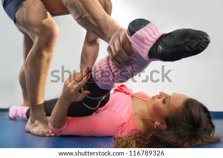 Male trainer helping girl to lying on straddle split on floor