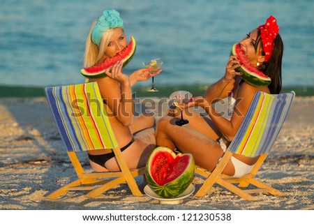 Young stylish ladies at sea with watermelon and a drink relaxing on deck chair