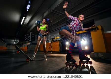 Portrait of two sexy friendly girls with boom box with cassette tape going to make party on roller skates and skate in modern car parking .