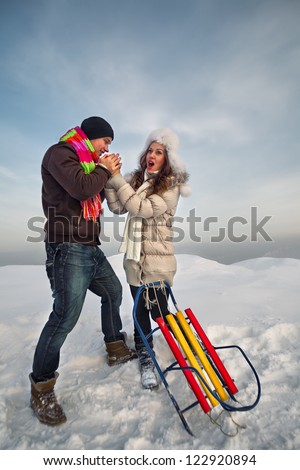 Bright picture of family couple in a winter clothes with sleigh. He warms her hands