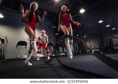 Muscular powerful Santa working out with rope and Santa helpers  jumping rope in functional training fitness gym