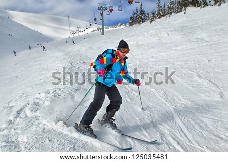 Young guy skier turning in powder snow; blue jacket; black pant