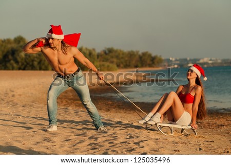 Santa pulling Sexy Santa girl on a sled at the beach.(concept: Tropical winter fun)