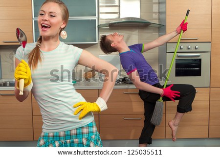 Modern kitchen - woman pretend to sing song with ladle and smiling young man cleaning the floor at home and play like guitar with  mop
