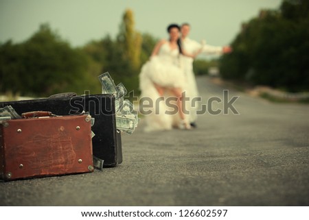 Young newlywed couple with suitcases of cash  hitchhiking on a road.