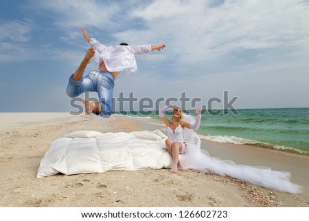 Happy Groom flying on bed to his bride on the beach