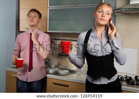Young man washing dishes and his girlfriend talking by mobile phone in kitchen