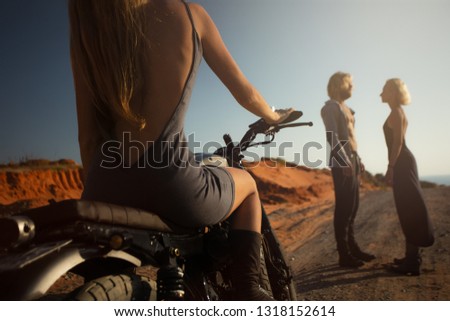 Sexy young women sit on motorcycle and looking at man Bearded man with other girl at sunset. Unfaithful love.