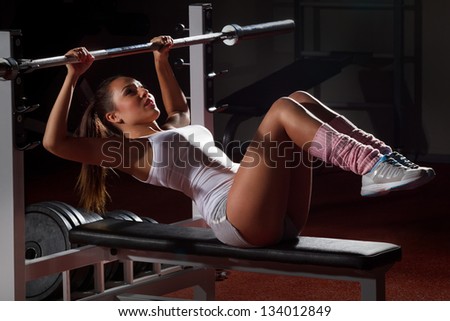 Beautiful girl in sports to a hall carries out exercise with a bar in the gym Bar Bench Press