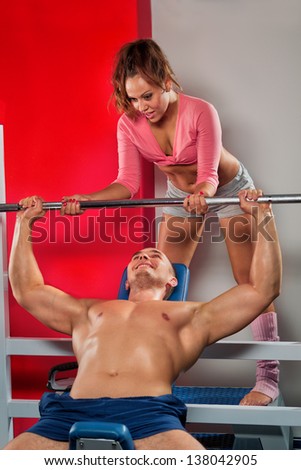 Female trainer helping guy to train in the gym Bar Bench Press