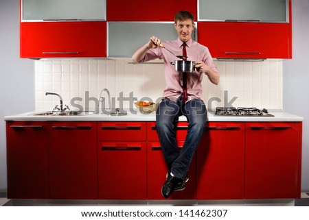 Portrait of  young hungry man filching  pan with soup on red kitchen