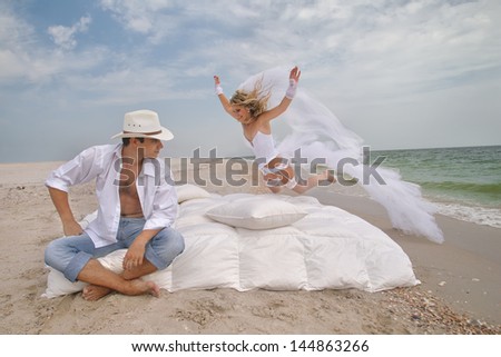 Happy bride flying on bed to her groom on the beach