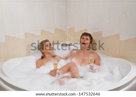 A young beautiful couple is enjoying a bath with champagne in a glass and looking at bubbles that are floating in the air