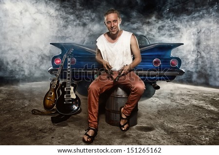 Guitarist at a garage next to the retro car in smoke