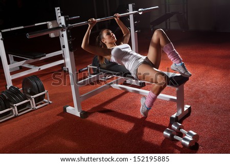 Beautiful girl in sports to a hall carries out exercise with a bar in the gym Bar Bench Press