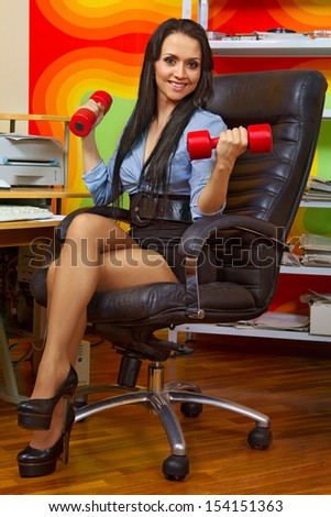 Office portrait of beautiful businesswoman stretching with dumbbells at her workplace