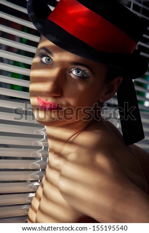 Cabaret performer in black top hat looking through a jalousie
