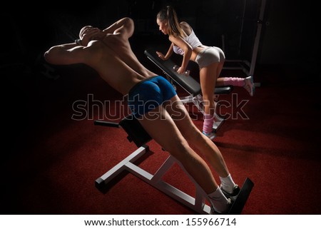 Young bodybuilder training his muscular back and  woman with dumbbells in sport centre