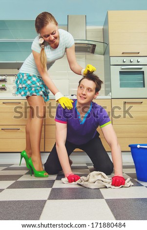 Young man cleaning floor and looking at his girlfriend