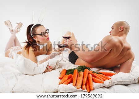Lovely couple in rabbit costume lying  in bed with  glass of red wine and carrots