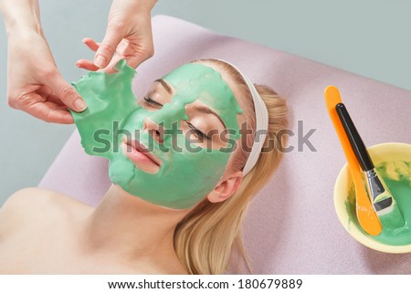 Young beautiful girl receiving facial green mask in spa beauty salon