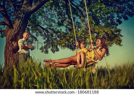 Beautiful girl on the swing in the forest with her parents Beautiful girl on the swing in the forest with her parents