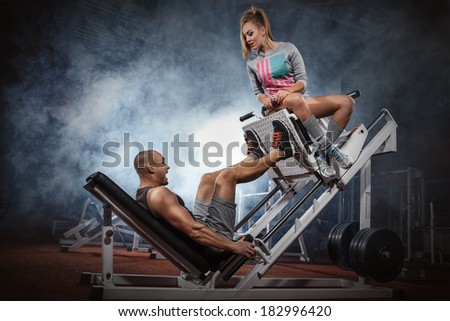 Man weightlifter doing leg presses with his trainer up on simulator
