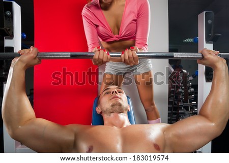 Female trainer helping guy to train in the gym Bar Bench Press