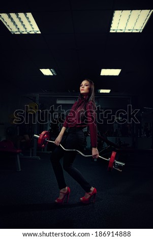 Portrait of beautiful young woman in a trouser suit doing exercise with weight bar