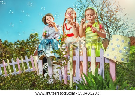 Cute little girls with boy are blowing a soap bubble