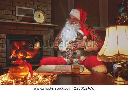 Santa Claus sitting with his cat at home near Christmas tree and  resting by his fireplace