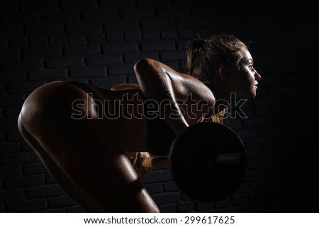 Strong young woman with beautiful athletic body doing exercises with barbell.