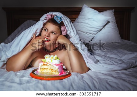 Portrait of beautiful plus size curly red hair young woman hiding under the blanket and eating sweet pastry in bed