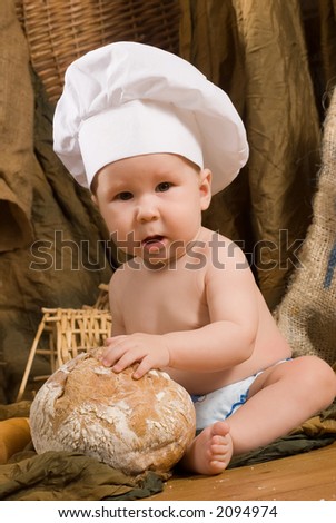 child with bread on bakery-like background wearing cook-hat