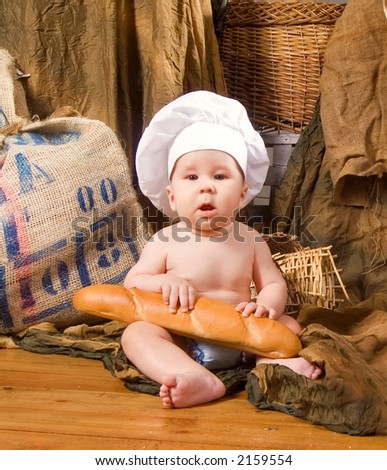 child with bread on bakery-like background wearing cook-hat